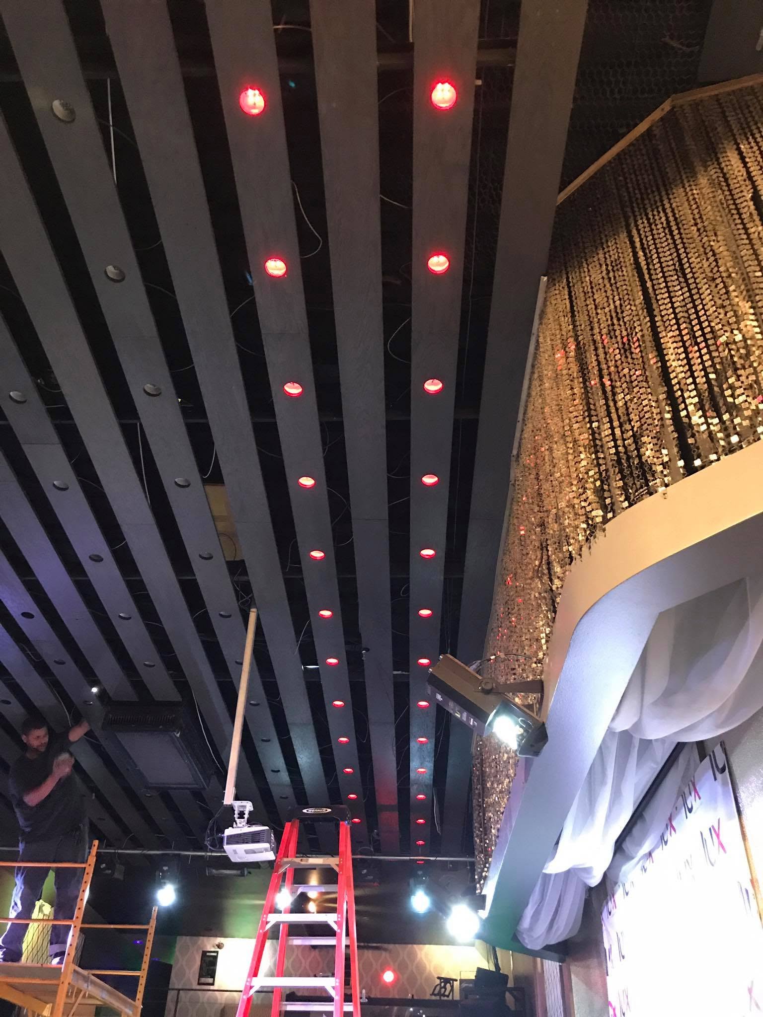 Technician and ladders beneath ceiling infrastructure during a venue installation