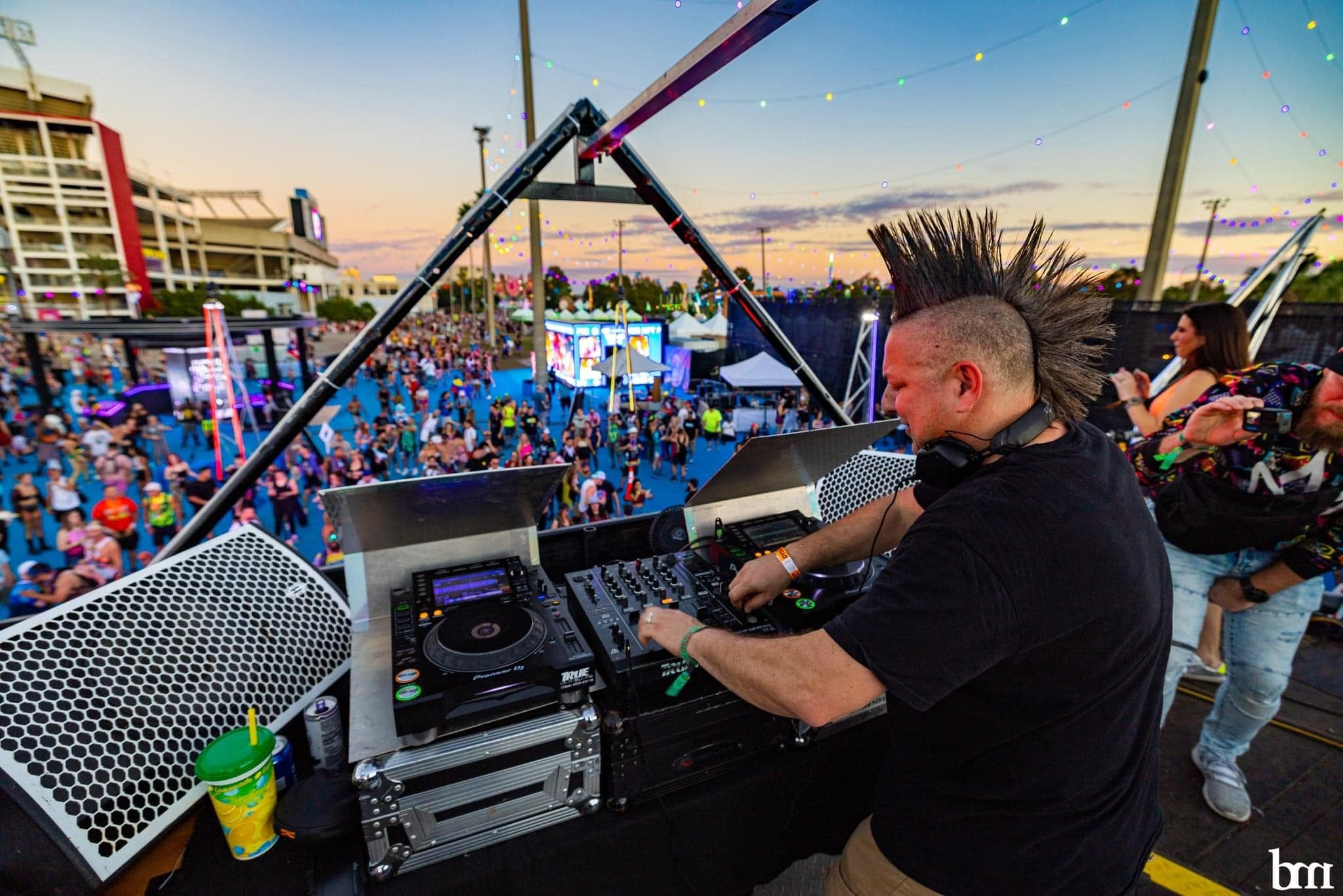 DJ overlooking an outdoor festival crowd at sunset